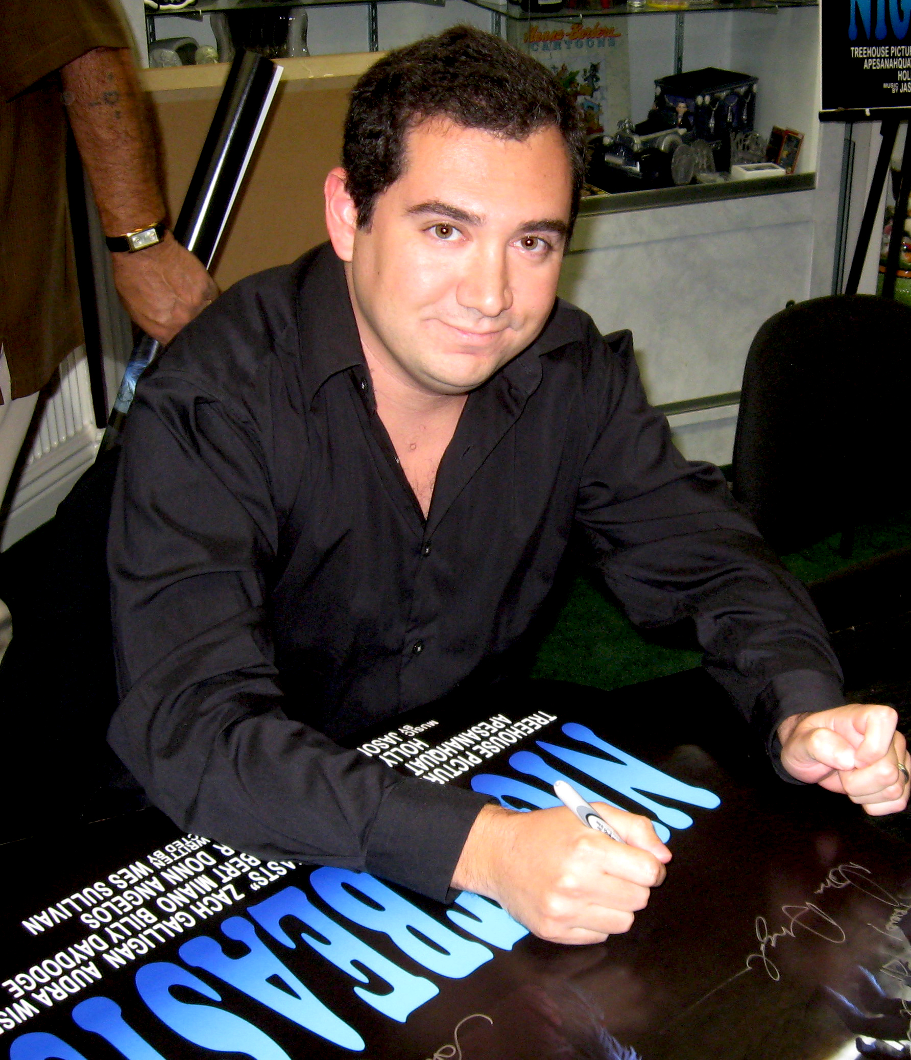 Jason Solowsky seated at a table, signing a Nightbeasts film poster