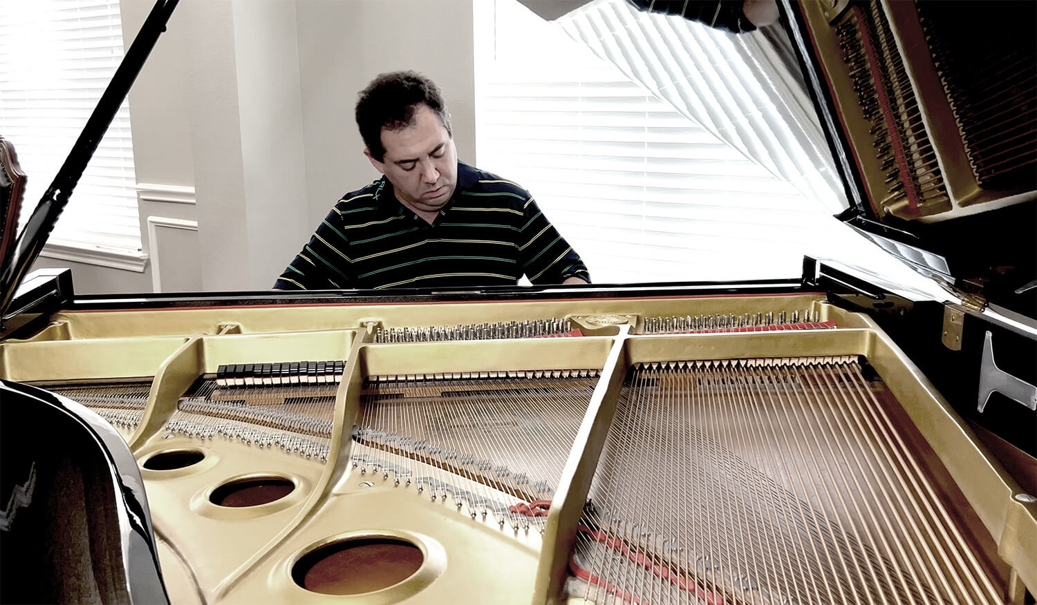 Jason Solowsky at the piano, seen over the open strings and gold frame of a grand piano